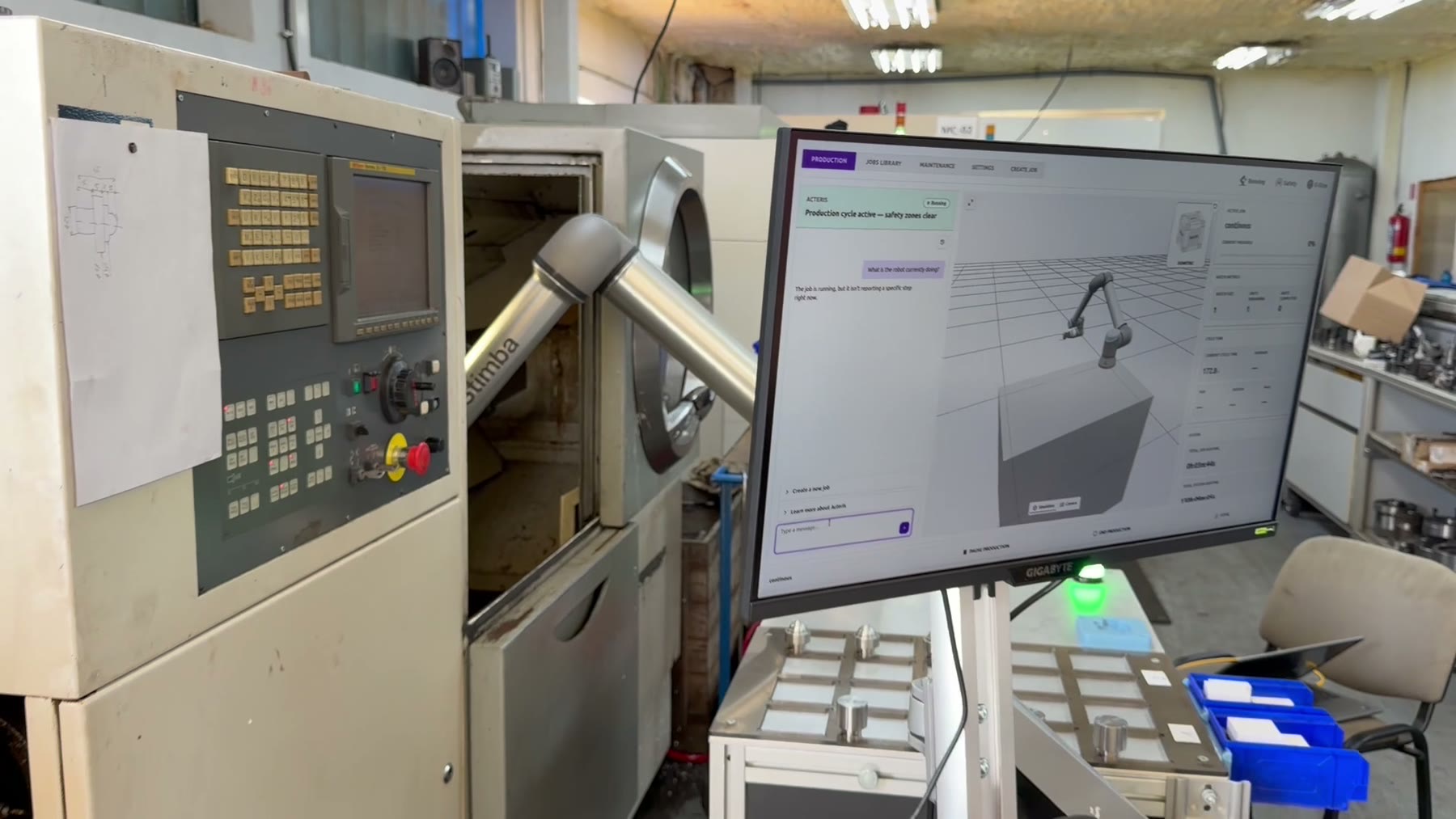 Monitor s rozhraním Acteris a 3D modelom robotickej bunky pri CNC sústruhu, v pozadí cobot UR